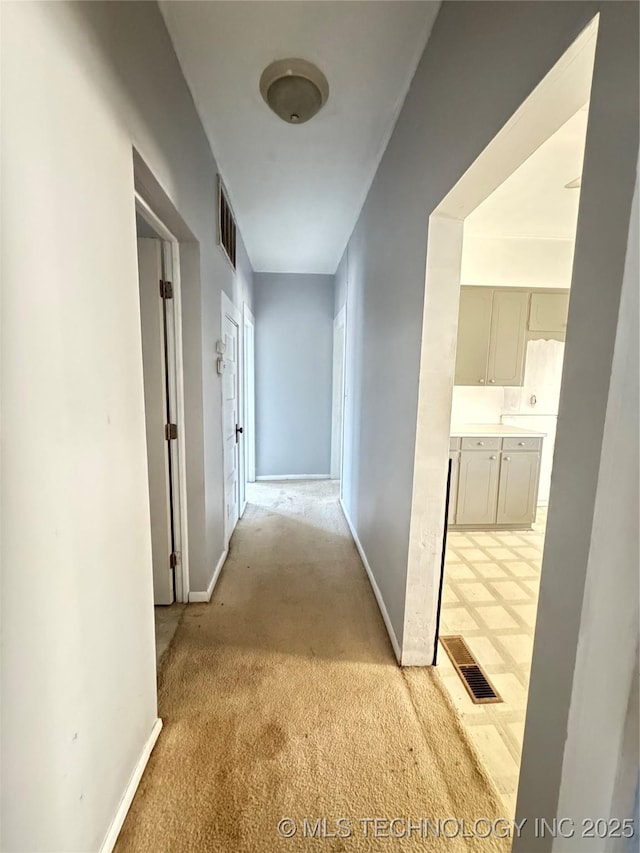 corridor featuring visible vents, baseboards, and light colored carpet