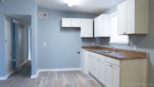 kitchen with visible vents, light wood-style flooring, a sink, dark countertops, and white cabinets