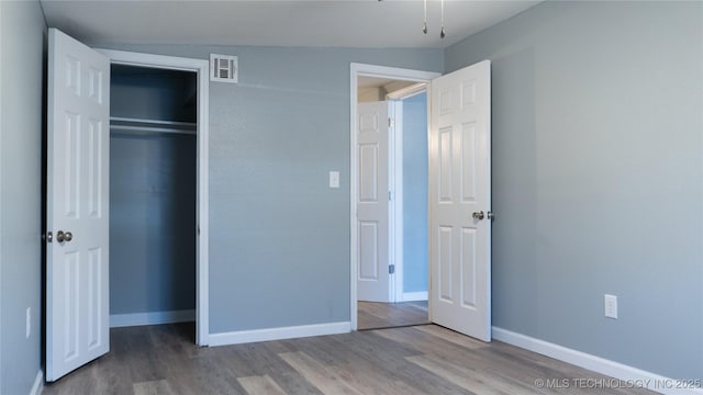 unfurnished bedroom with visible vents, baseboards, a closet, and wood finished floors