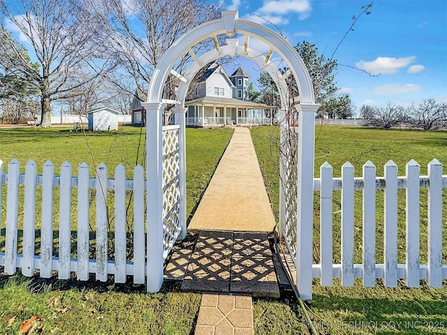 view of gate featuring a yard, covered porch, and a fenced front yard