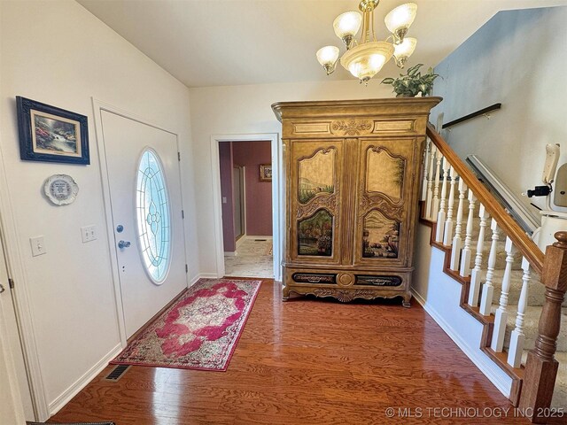 entryway with visible vents, wood finished floors, an inviting chandelier, baseboards, and stairs