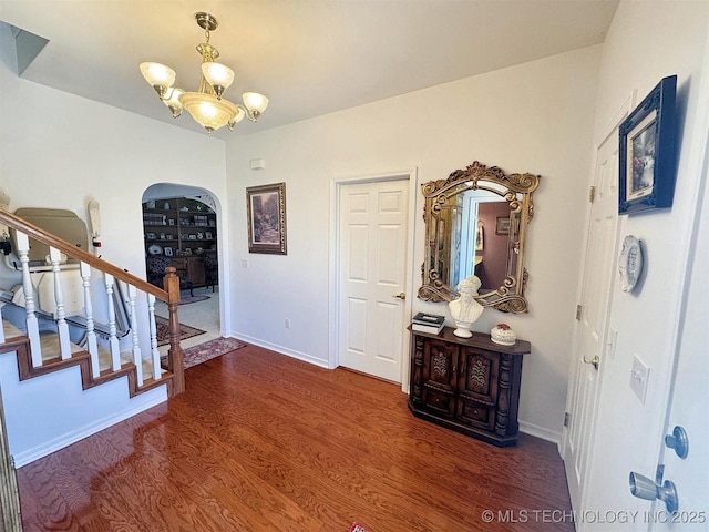 foyer entrance featuring stairway, wood finished floors, baseboards, arched walkways, and a chandelier