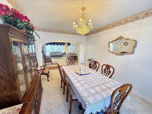 carpeted dining space with baseboards, arched walkways, and a chandelier