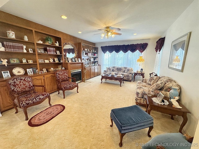 sitting room featuring built in shelves, light carpet, recessed lighting, a glass covered fireplace, and a ceiling fan