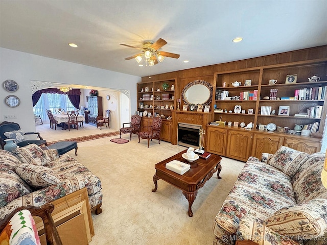 living room with built in features, light colored carpet, recessed lighting, a fireplace, and a ceiling fan