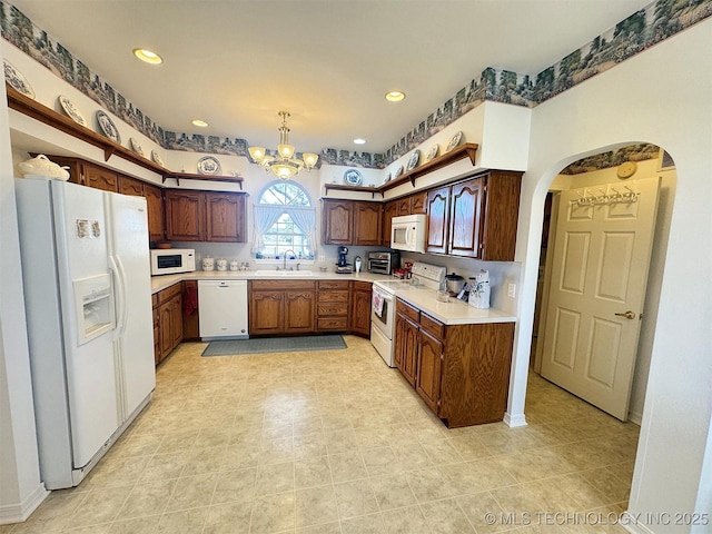 kitchen featuring a sink, white appliances, arched walkways, and light countertops