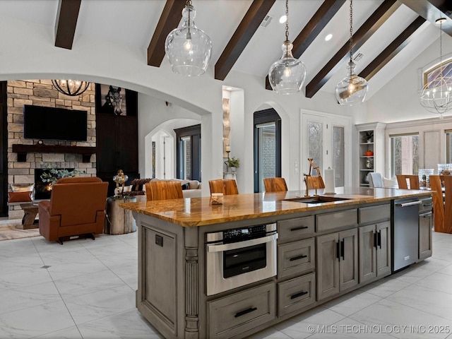 kitchen with an island with sink, arched walkways, oven, a stone fireplace, and open floor plan