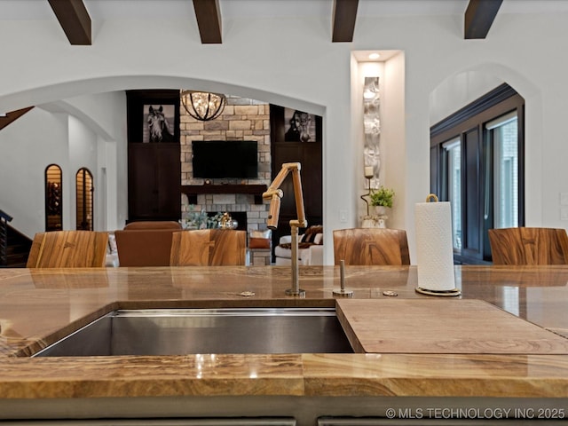 kitchen with wood counters, beam ceiling, arched walkways, and a fireplace