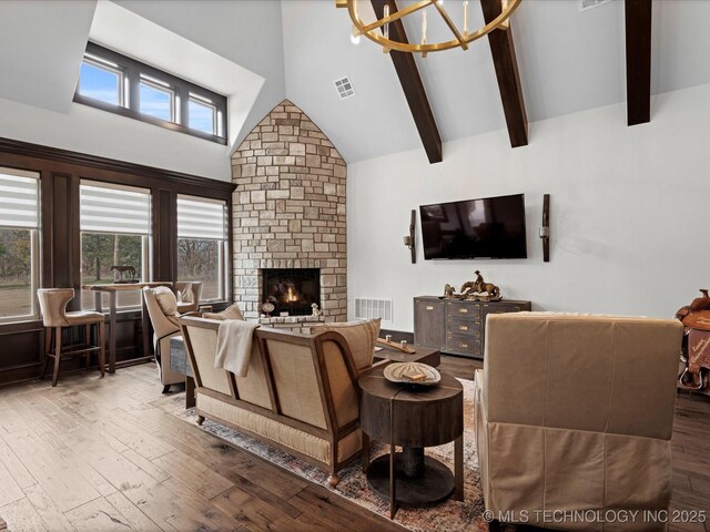 living room featuring visible vents, beam ceiling, high vaulted ceiling, wood finished floors, and a stone fireplace