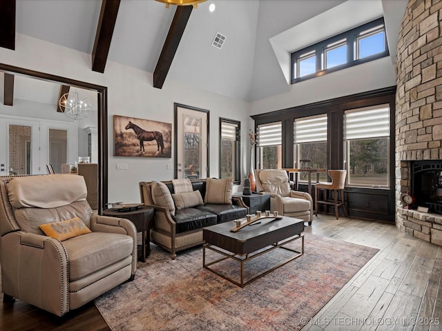 living room with visible vents, high vaulted ceiling, beam ceiling, a stone fireplace, and wood-type flooring