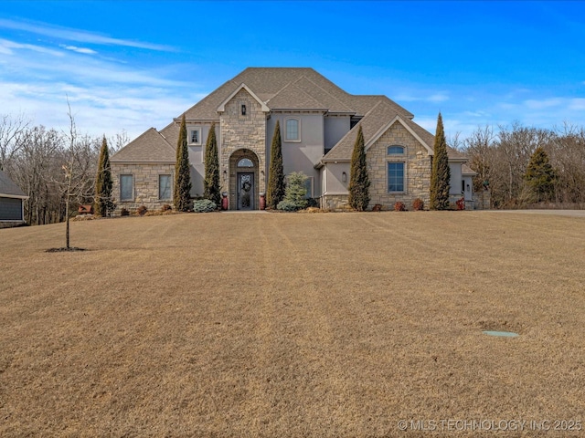 french country style house featuring a front yard, stone siding, and stucco siding