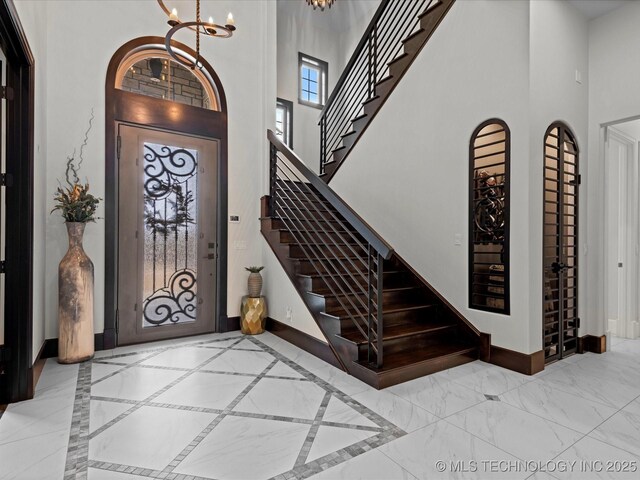 entrance foyer featuring baseboards, stairway, a high ceiling, an inviting chandelier, and marble finish floor