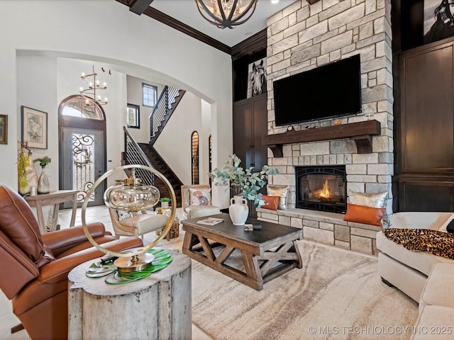 living area with stairway, ornamental molding, a stone fireplace, a high ceiling, and a notable chandelier