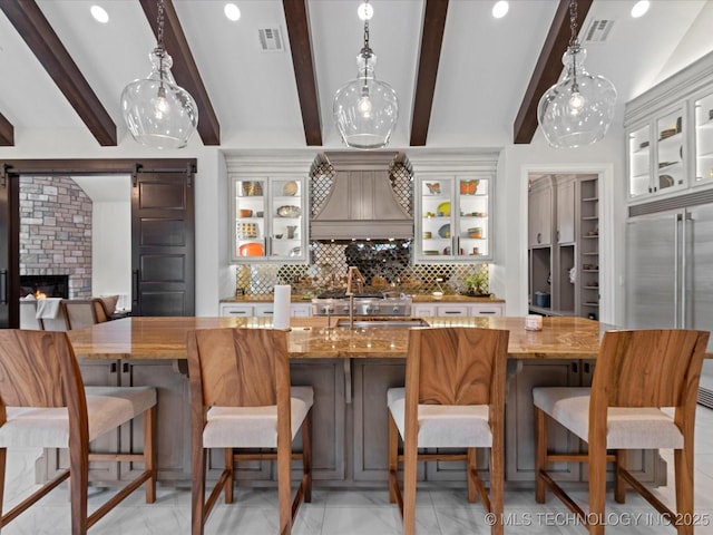 kitchen featuring tasteful backsplash, visible vents, stainless steel built in refrigerator, a barn door, and custom exhaust hood