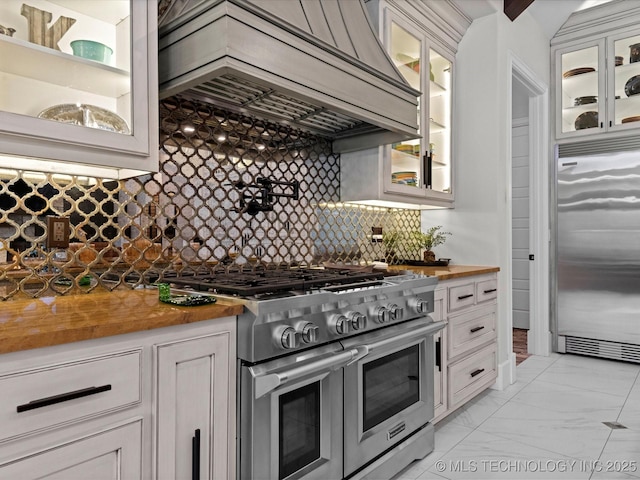 kitchen with butcher block countertops, high quality appliances, custom range hood, white cabinets, and marble finish floor