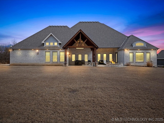 view of front of house with brick siding, a patio, and roof with shingles