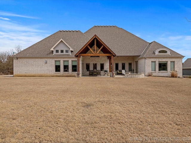 rear view of house featuring a patio area, brick siding, and roof with shingles