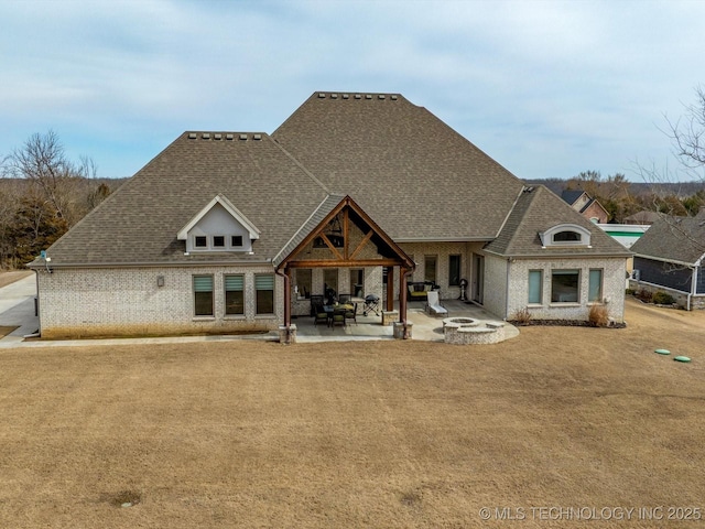 back of property with a patio area, an outdoor fire pit, roof with shingles, and brick siding