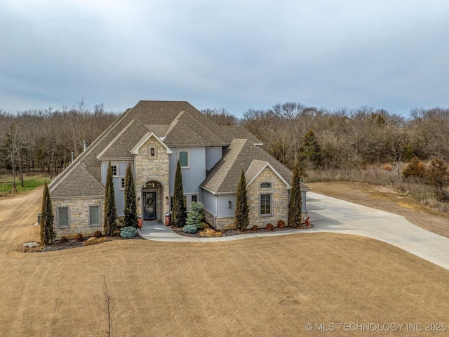 view of front of property with a front lawn, stone siding, and roof with shingles