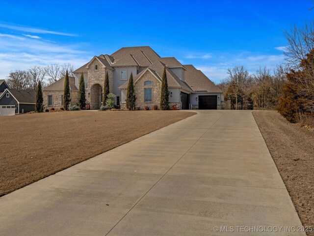 french country inspired facade featuring stone siding, a garage, concrete driveway, and a front yard