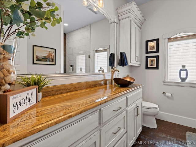 bathroom with toilet, wood finished floors, a tile shower, baseboards, and vanity