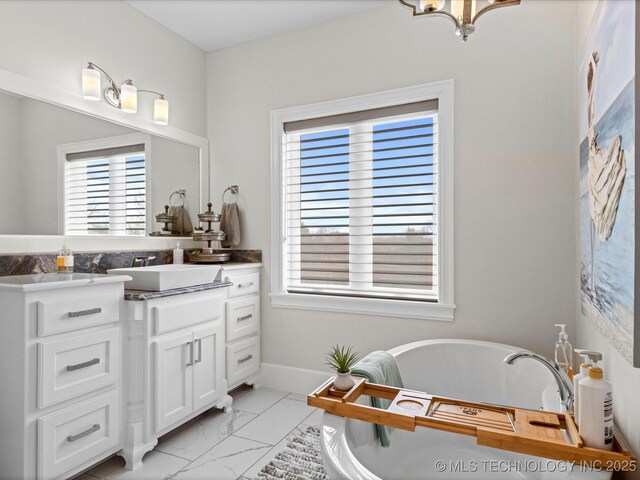 bathroom featuring marble finish floor, a freestanding bath, vanity, and baseboards