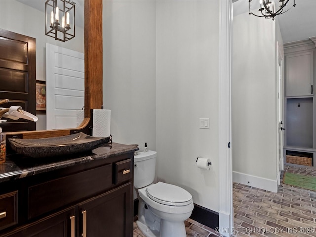 bathroom featuring vanity, baseboards, brick floor, toilet, and a chandelier