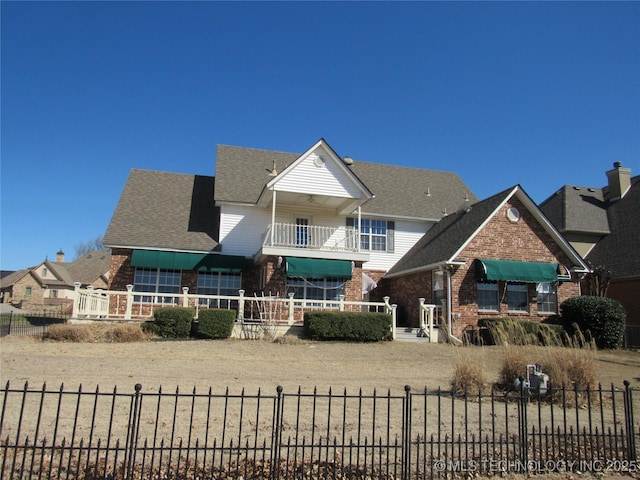 view of front of property featuring brick siding, a shingled roof, and fence