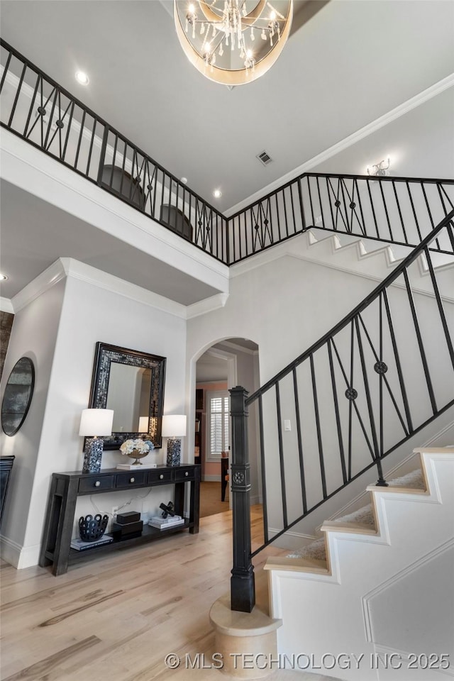 stairs featuring wood finished floors, visible vents, a high ceiling, arched walkways, and ornamental molding