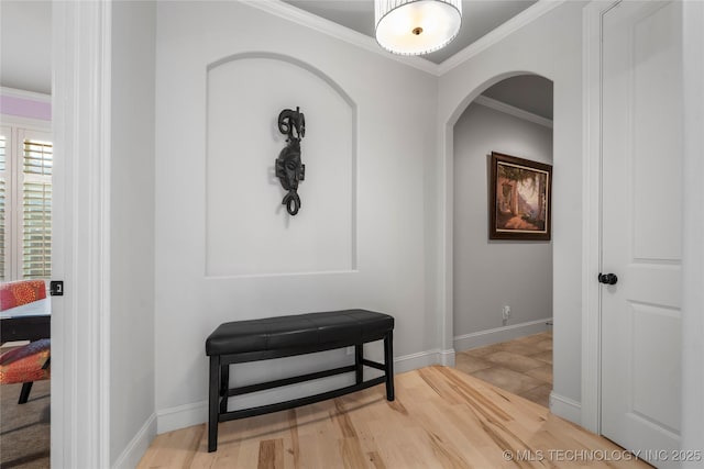 hall featuring crown molding, light wood-style floors, baseboards, and arched walkways