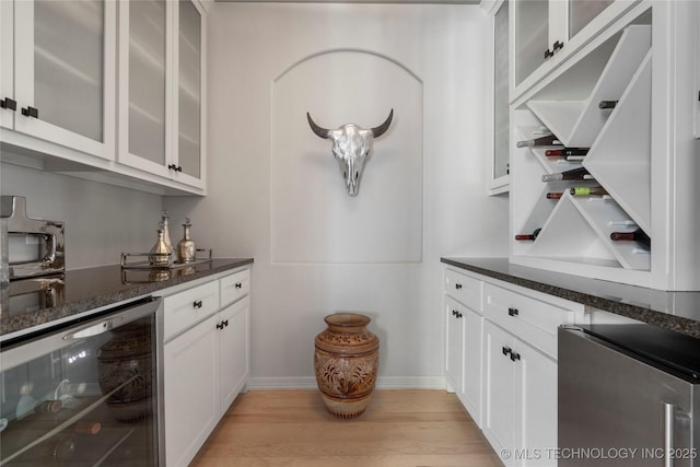 bar with a bar, light wood-style flooring, beverage cooler, and baseboards