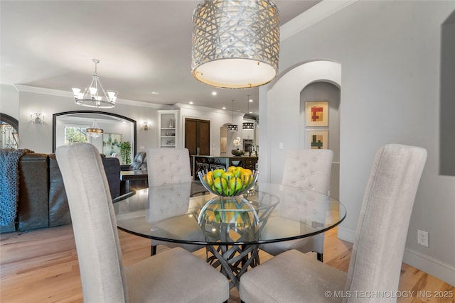 dining area featuring crown molding, light wood-style flooring, and arched walkways