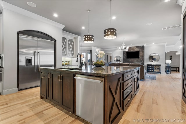 kitchen with a sink, appliances with stainless steel finishes, a center island with sink, and crown molding