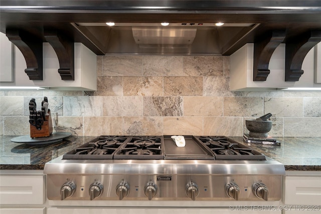 kitchen featuring dark stone countertops, stainless steel gas cooktop, decorative backsplash, white cabinets, and wall chimney exhaust hood