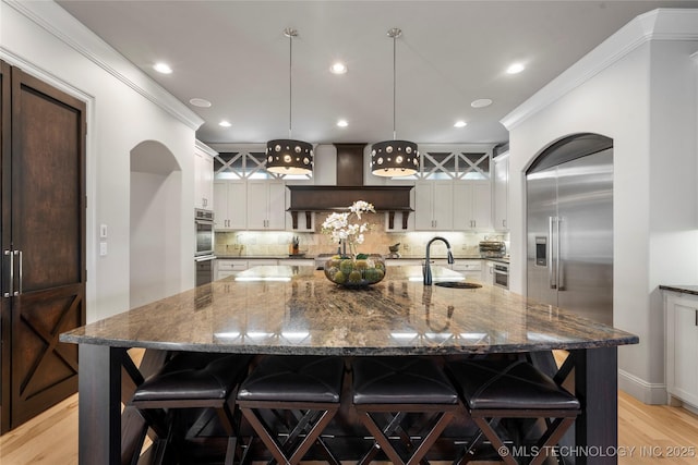 kitchen featuring premium range hood, a large island, a sink, a kitchen breakfast bar, and decorative backsplash