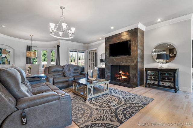 living room with wood finished floors, recessed lighting, ornamental molding, a tiled fireplace, and a notable chandelier