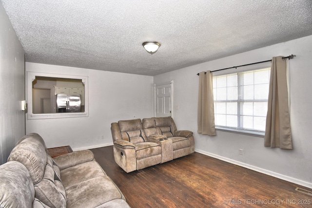 living room with visible vents, baseboards, a textured ceiling, and wood finished floors