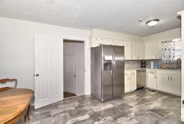 kitchen featuring a sink, light countertops, appliances with stainless steel finishes, white cabinetry, and backsplash