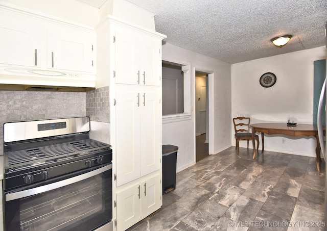 kitchen featuring baseboards, stainless steel range with gas cooktop, white cabinets, under cabinet range hood, and tasteful backsplash