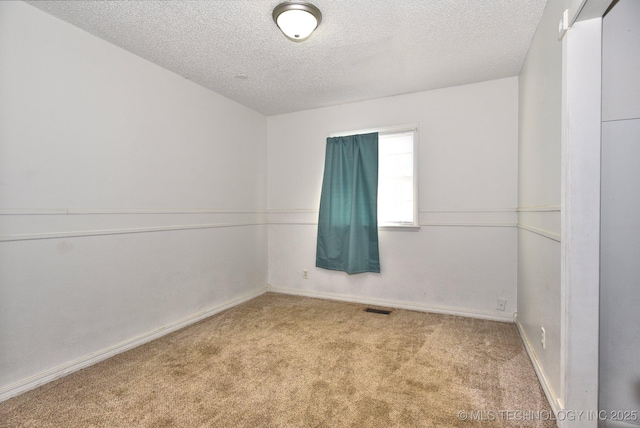 unfurnished room with visible vents, a textured ceiling, baseboards, and carpet floors