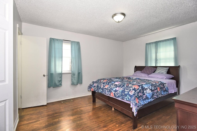 bedroom featuring baseboards, wood finished floors, visible vents, and a textured ceiling