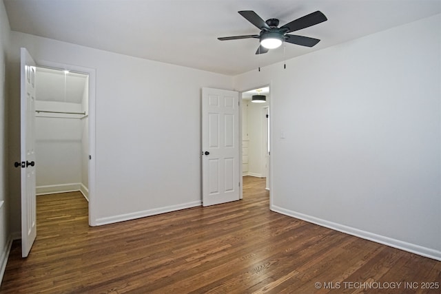 unfurnished bedroom featuring a closet, a walk in closet, baseboards, and wood finished floors