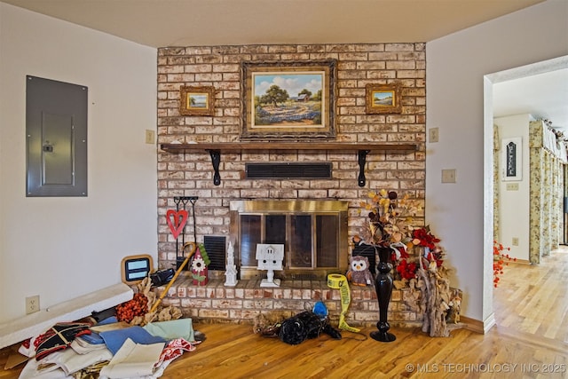 living area with wood finished floors, visible vents, baseboards, electric panel, and a brick fireplace