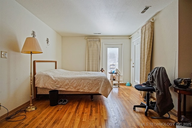 bedroom featuring visible vents, a textured ceiling, wood finished floors, and access to outside