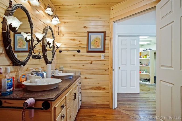 bathroom with double vanity, wood finished floors, a sink, and wood walls