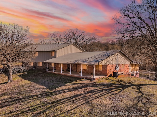 back of house at dusk with metal roof, brick siding, a yard, and a patio area