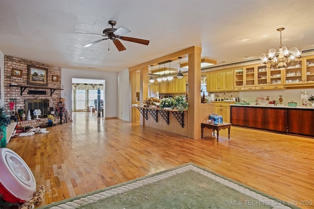 interior space featuring a brick fireplace, glass insert cabinets, open floor plan, and light wood finished floors