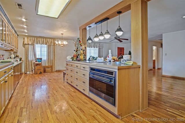 kitchen with stainless steel oven, light wood-type flooring, and hanging light fixtures