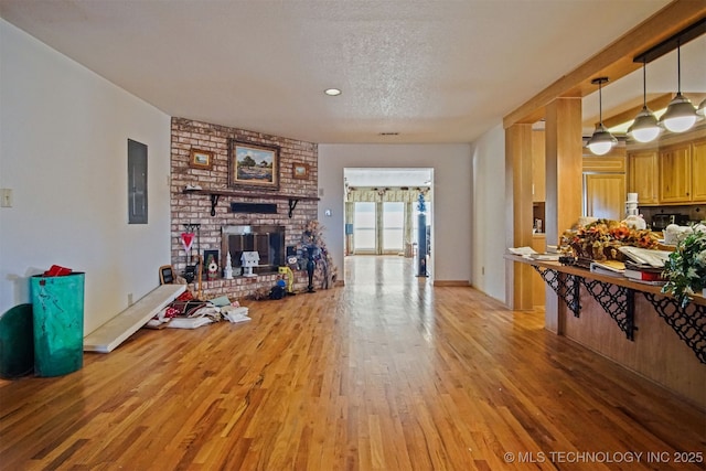 living room with a brick fireplace, light wood-style floors, baseboards, and a textured ceiling