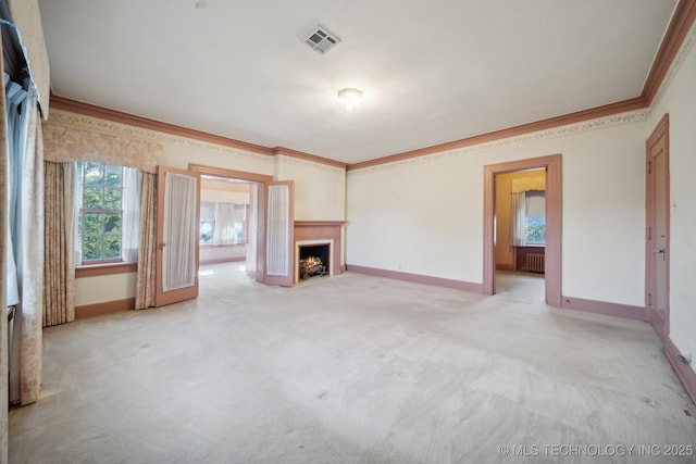 unfurnished living room with radiator, visible vents, a lit fireplace, crown molding, and light colored carpet